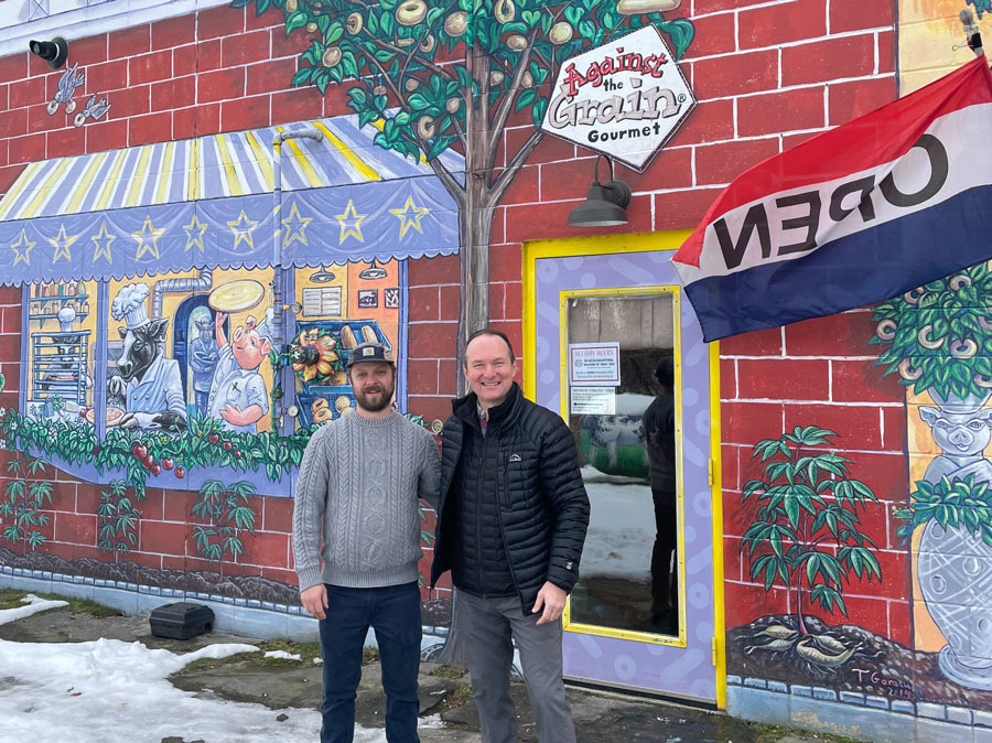 two smiling men standing in front of a brightly painted building||||||