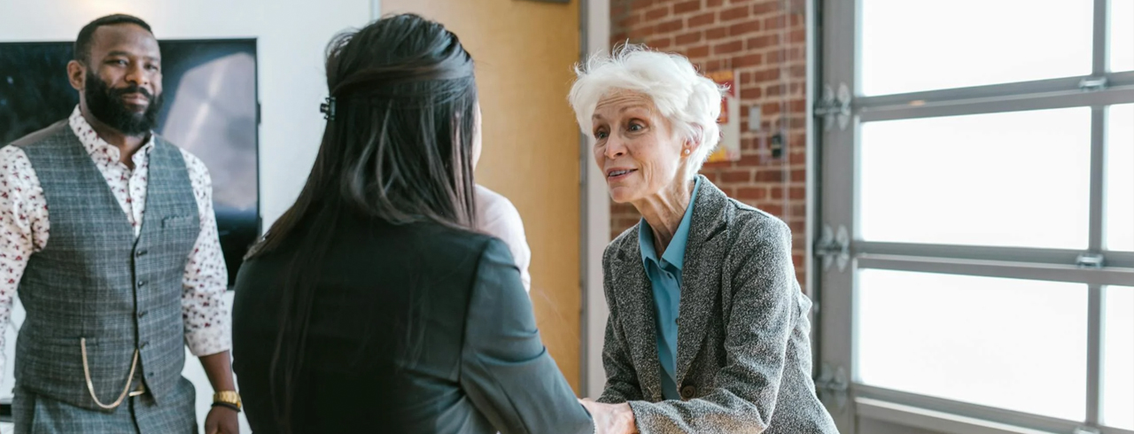 two women shaking hands while a man looks on